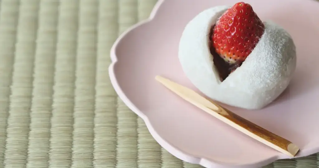 いちご大福がピンクの皿に乗った画像。大福からいちごが飛び出ている。